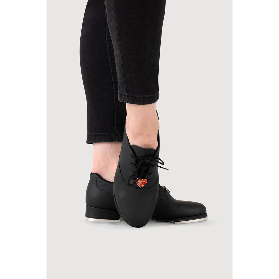 Black lace-up ankle boots with a small red heart charm, shown on a model wearing black cropped jeans against a light gray background.