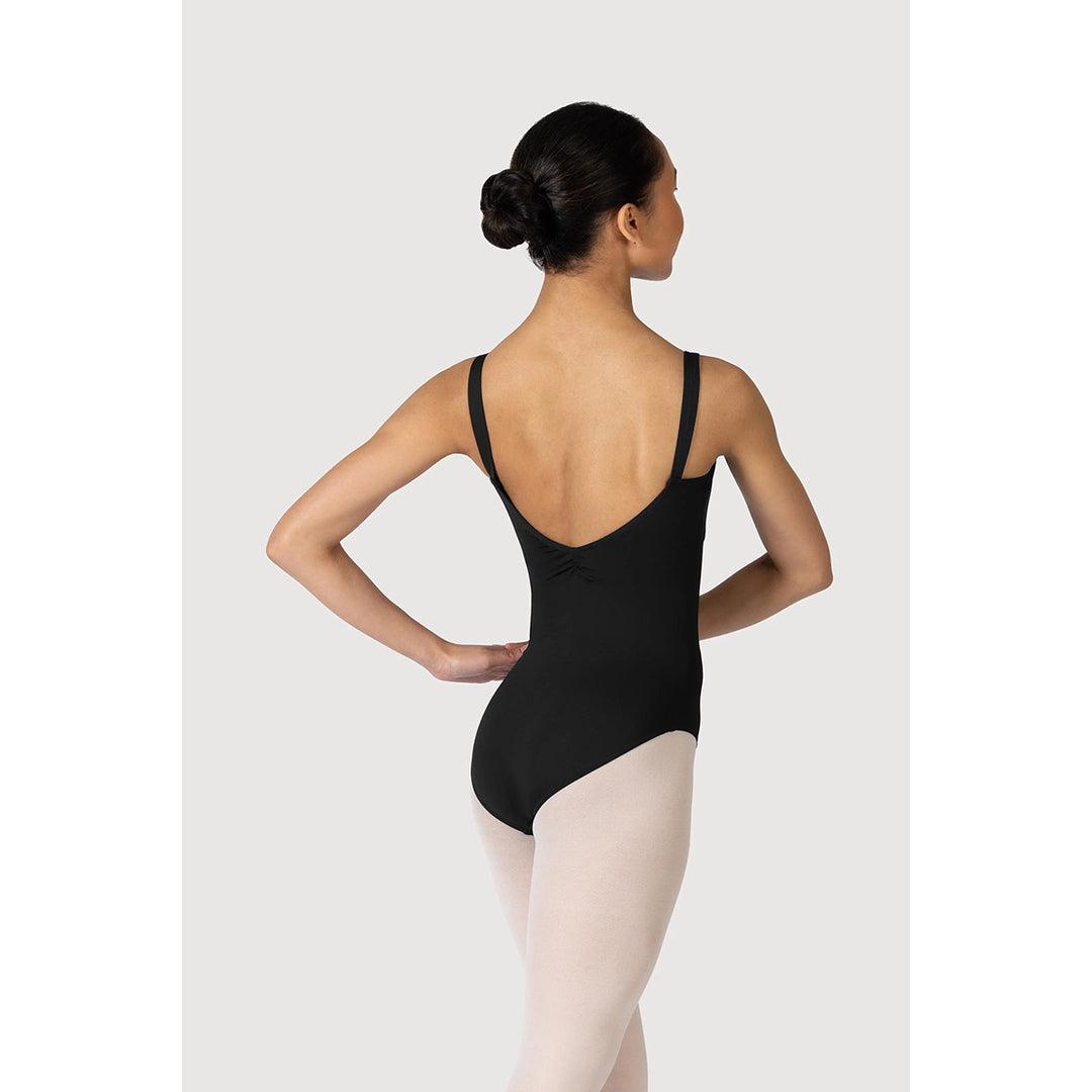 A woman modeling a black ballet leotard from the back, paired with light pink tights, against a light gray studio background.