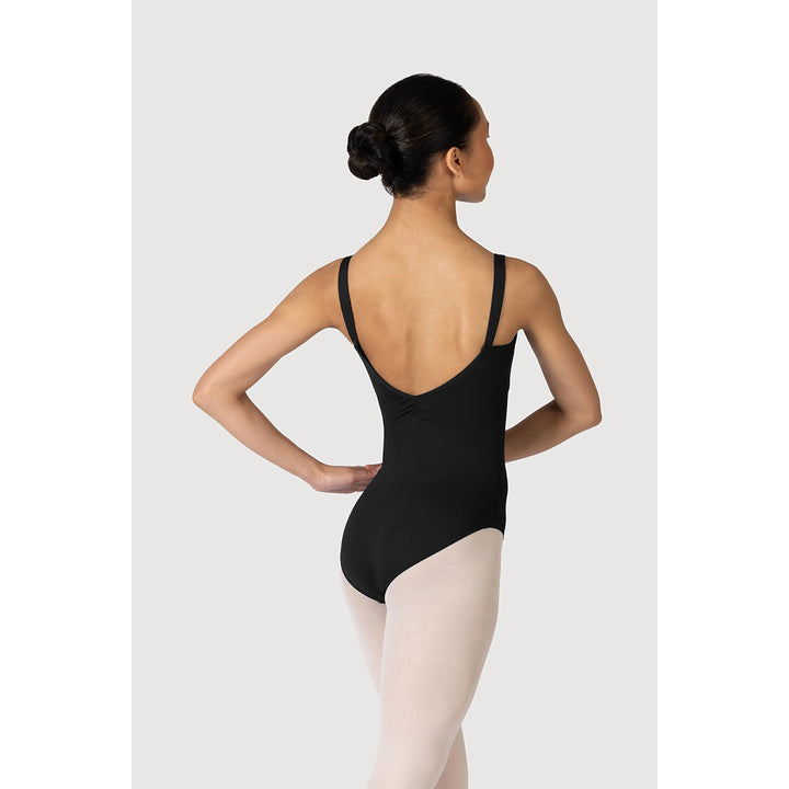 A woman modeling a black ballet leotard from the back, paired with light pink tights, against a light gray studio background.