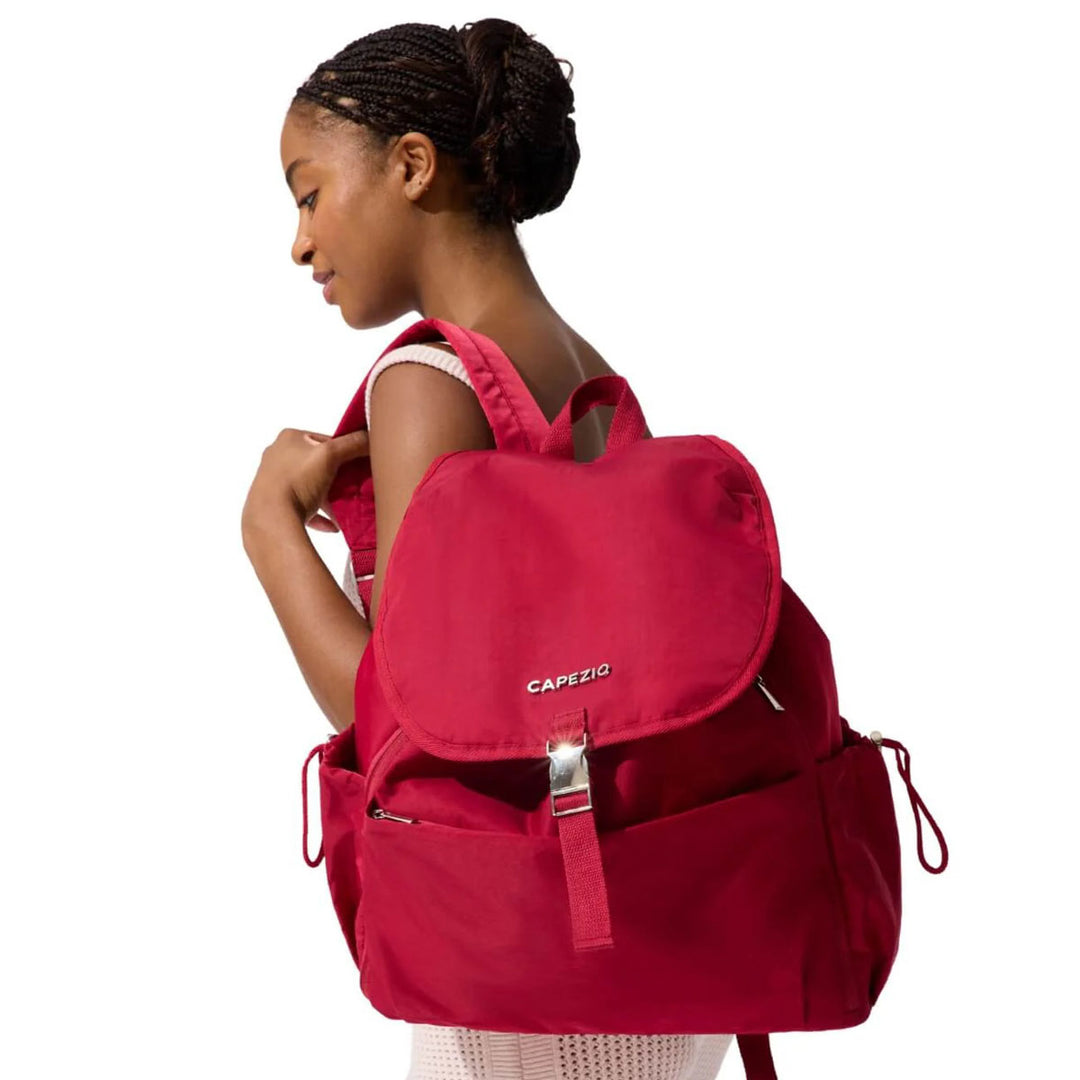 A woman shown from the back wearing a bright red backpack with a flap closure and silver zipper hardware. The brand name 'CAPEZIO' is printed in white on the front of the backpack.