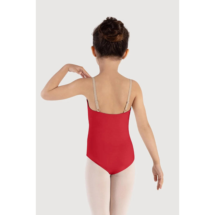 A young girl viewed from behind wearing a bright red ballet leotard with beige shoulder straps and light pink tights, set against a plain light gray studio background.