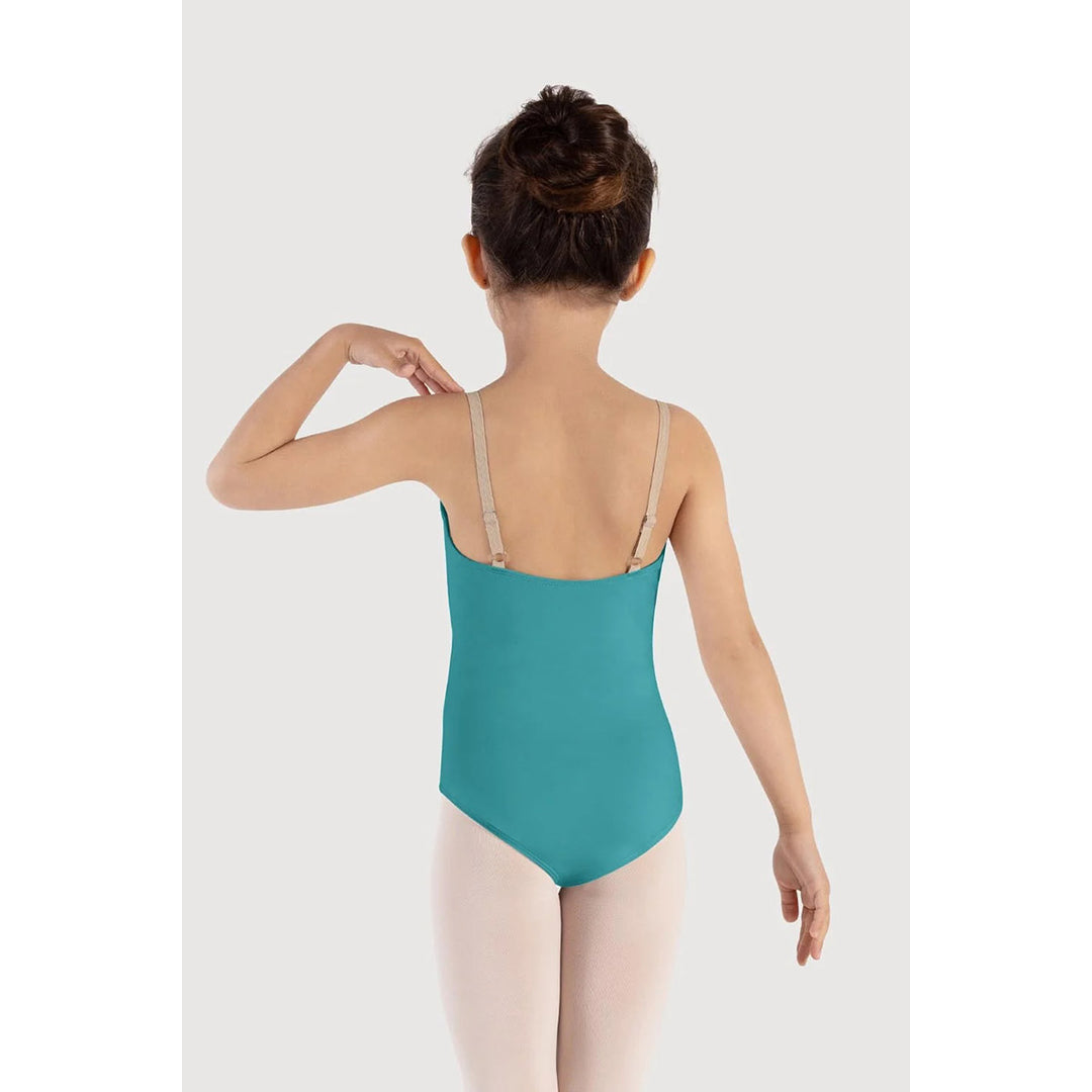 A young girl is shown from behind wearing a teal blue leotard with beige shoulder straps, paired with light pink tights, against a light gray studio background.
