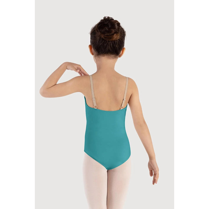 A young girl is shown from behind wearing a teal blue leotard with beige shoulder straps, paired with light pink tights, against a light gray studio background.