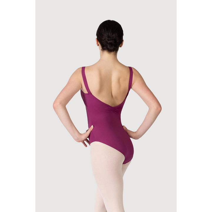 A woman viewed from the back wearing a deep magenta dance leotard and light pink tights against a light gray studio background.