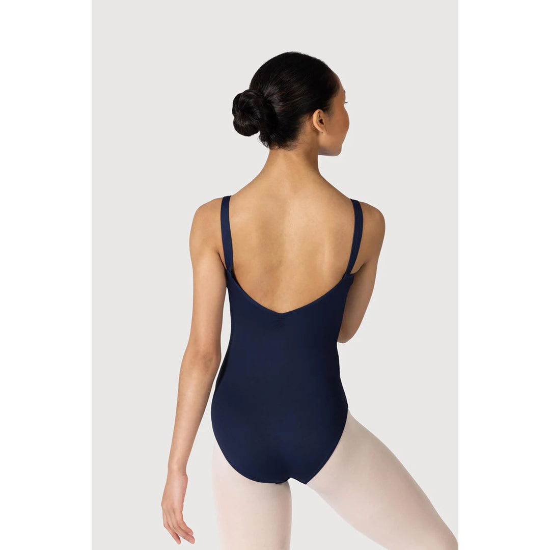 A woman modeling a navy blue leotard from the back, wearing light pink tights against a light gray studio background.