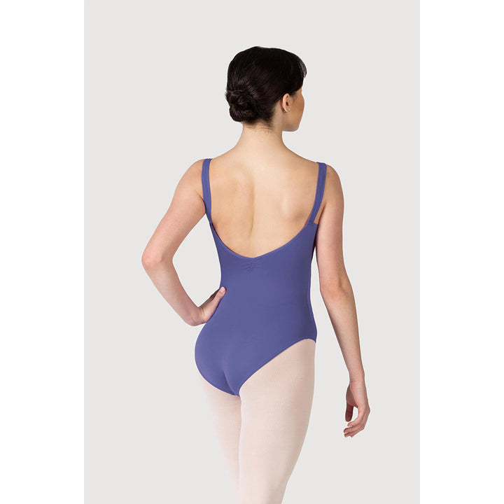 A woman modeling a slate blue-purple leotard from the back, paired with light pink tights, against a light gray studio background.