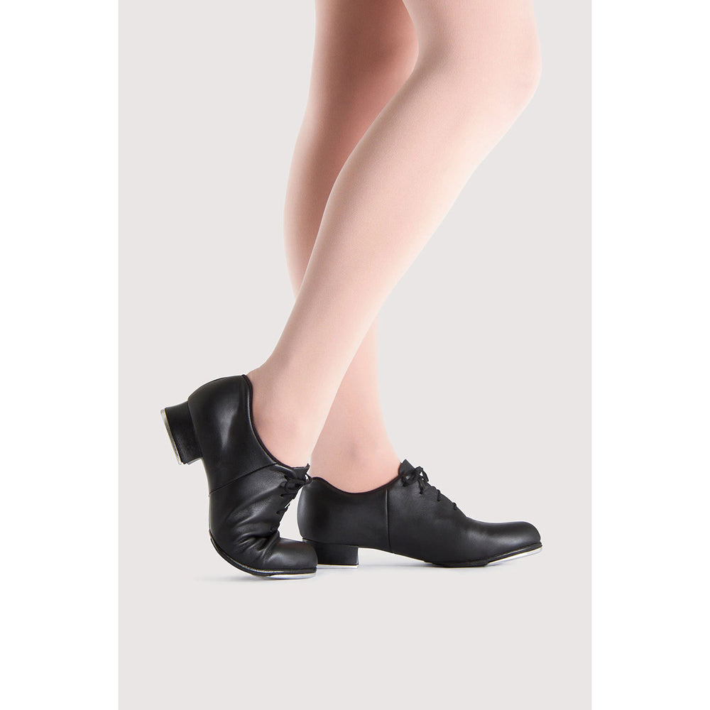 Black leather dance shoes with low block heels and lace-up fronts, shown on a model's feet against a light gray background.