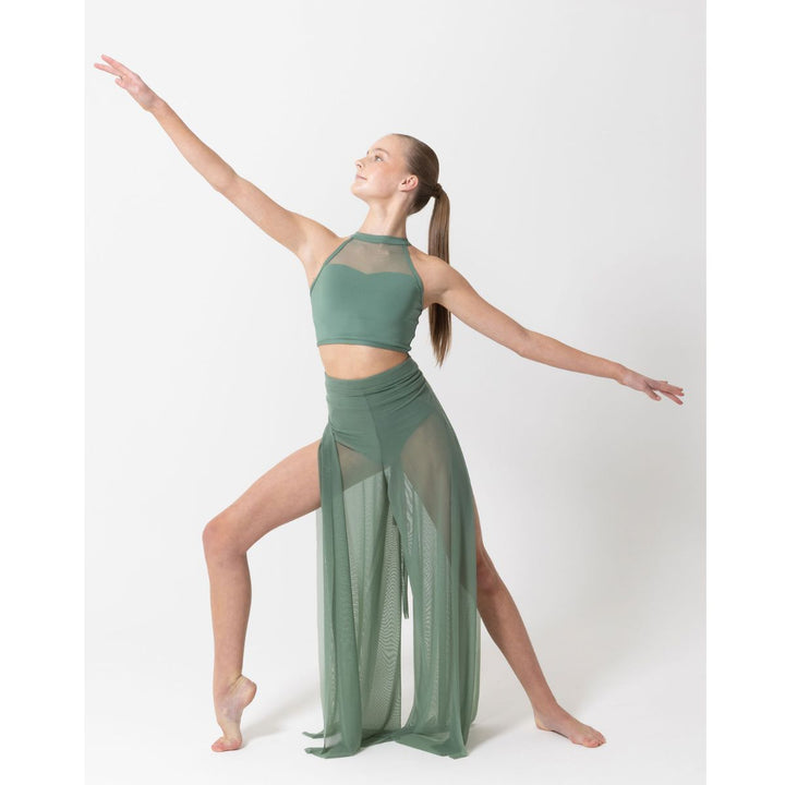 A woman in a sage green two-piece activewear set with sheer mesh panels, posing dynamically with arms outstretched against a light gray studio background.