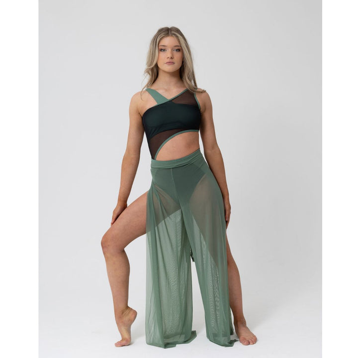 A woman modeling a two-piece activewear set consisting of a black and sage green cutout sports bra and matching sage green sheer wide-leg pants, posed against a light gray studio background.