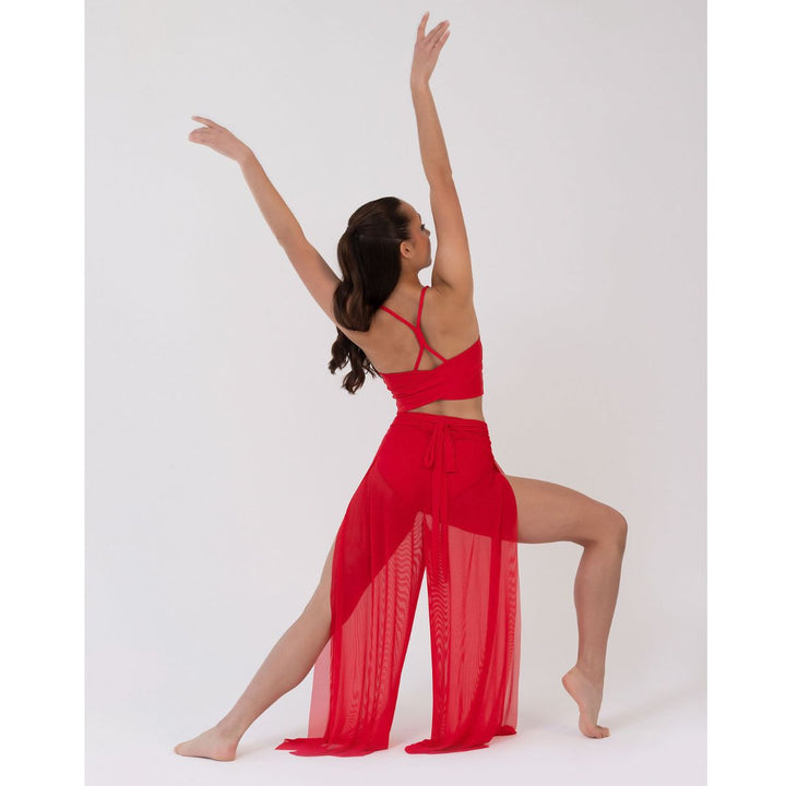 A woman in a bright red two-piece outfit poses dynamically with her arms raised against a plain light gray studio background.