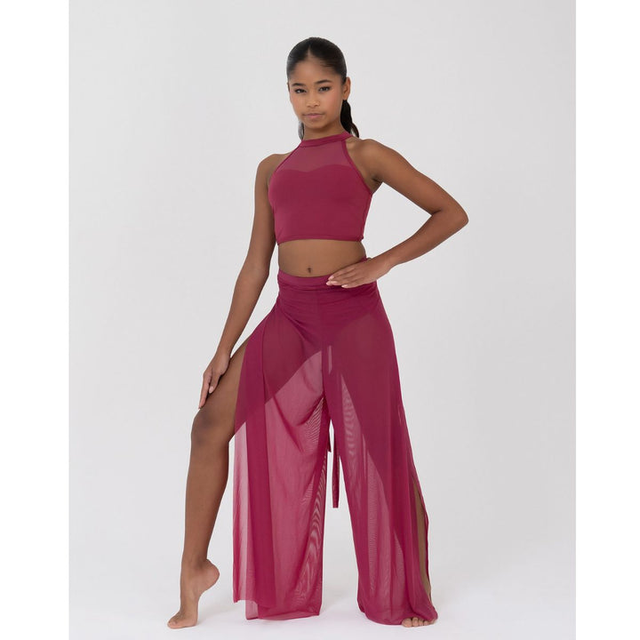 A woman modeling a matching two-piece activewear set in a deep magenta color, featuring a high-neck crop top and sheer wide-leg pants, against a plain light gray studio background.